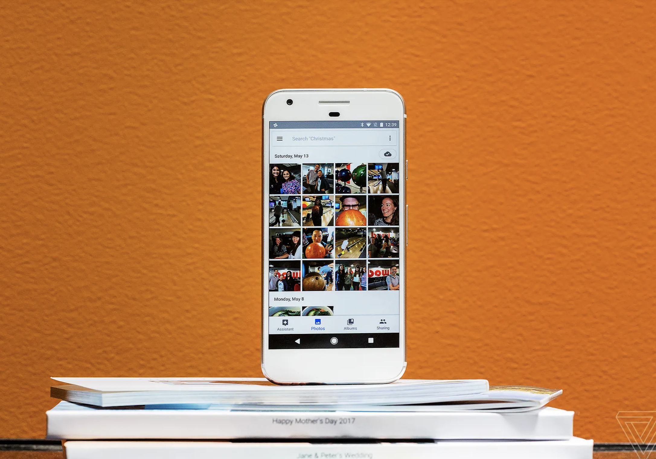 An iphone displaying grid of images, standing on top of a stack of paper